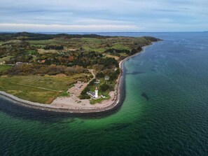 An aerial view of a coastal area with a lighthouse, a small parking lot, and a road leading to the shore. - Holiday Home in Knebel (Knebel)