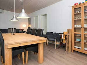 Un comedor con mesa de madera, sillas negras, lámparas colgantes y un mueble con vajilla.
