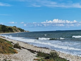 A coastal landscape with a rocky shoreline, waves, and a distant landmass under a clear sky.