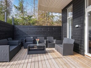 En udendørs patio med mørkt fletmøbel, et glasbord og en træterrasse.