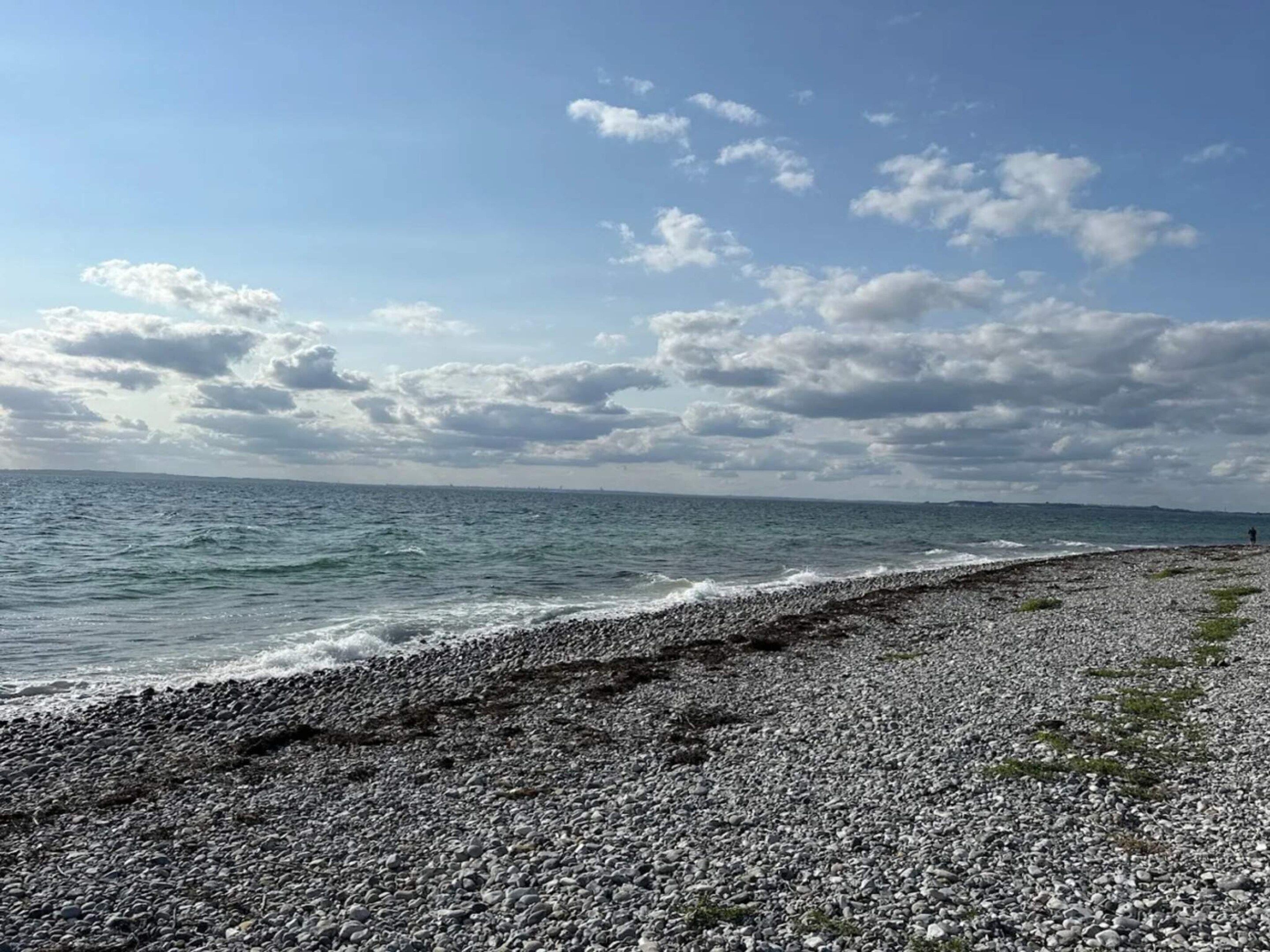 A pebbled beach with a view of the sea and a distant shoreline.