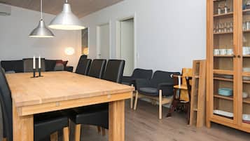 A dining area with a wooden table, black chairs, pendant lights, and a wooden cabinet with glass doors.