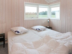 A bedroom with a bed, two pillows, a nightstand, and a window with a view of trees. - Holiday Home in Hadsund (Hadsund)