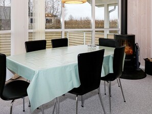 Un coin repas avec une table dressée pour six personnes, entouré de chaises noires, d’une cheminée et de grandes fenêtres donnant sur l’extérieur.