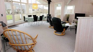 A spacious room with a large table and chairs, a wicker chair, a television, and a potted plant. - Holiday Home in Hadsund (Hadsund)