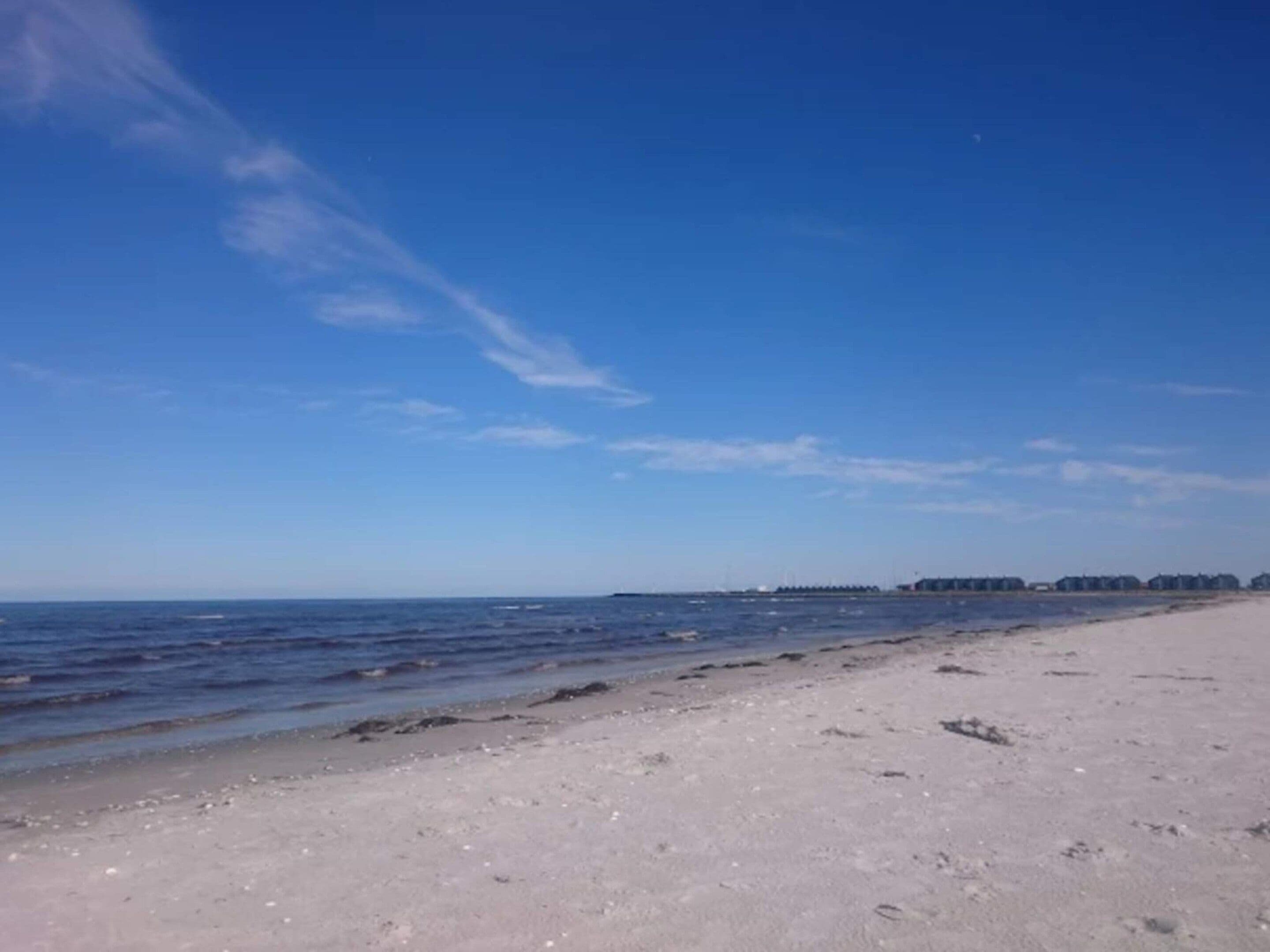 A beach with a clear sky, calm sea, and distant buildings.