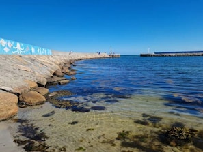 A rocky shoreline with clear water, a pier, and a blue wall with white text.