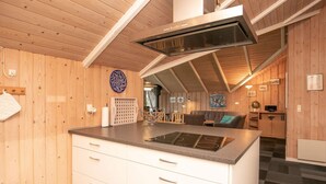 A modern kitchen with wooden walls, a central island with a built-in stove, and a ceiling with exposed beams. - 8 Person Holiday Home in Skals (Skals)