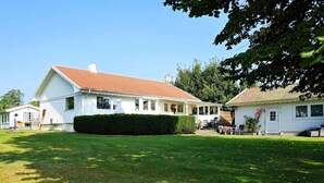 A white building with a red roof, a covered porch, and a well-maintained lawn. - Holiday Home in Ã…sa (Åsa)