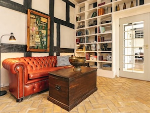 A room with a leather sofa, a wooden chest, a bookshelf, and a framed picture on the wall.