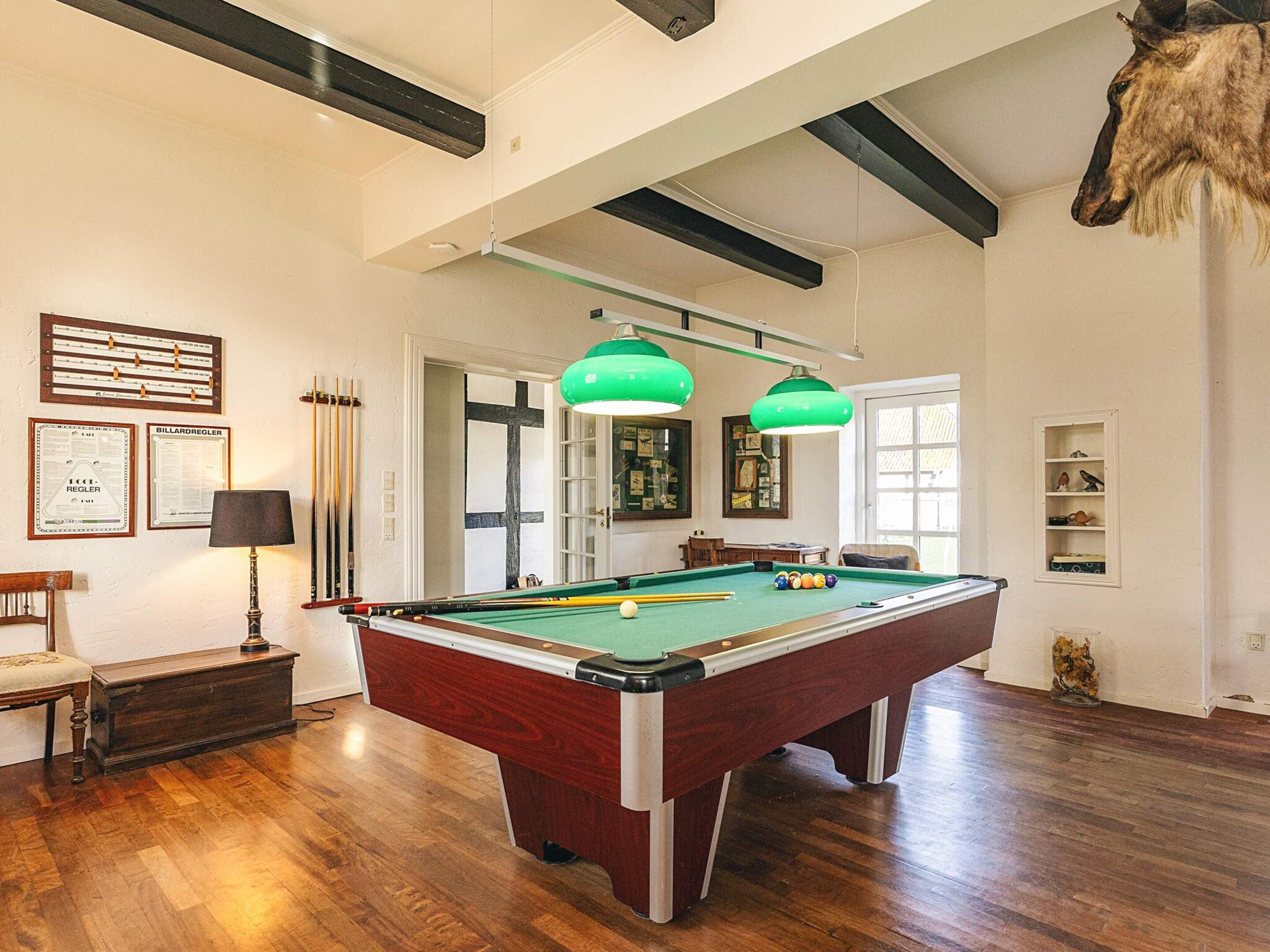 A pool table in a room with wooden flooring, a lamp, and a trophy.