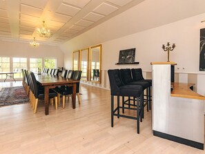 A spacious dining area with a long wooden table and black chairs, a bar area with stools, and large windows allowing natural light. - Holiday Home in Svendborg (Svendborg)