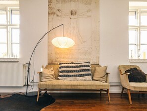 Una habitación con un sofá, una silla, una l ámpara de pie y una pared decorada con un dibujo.