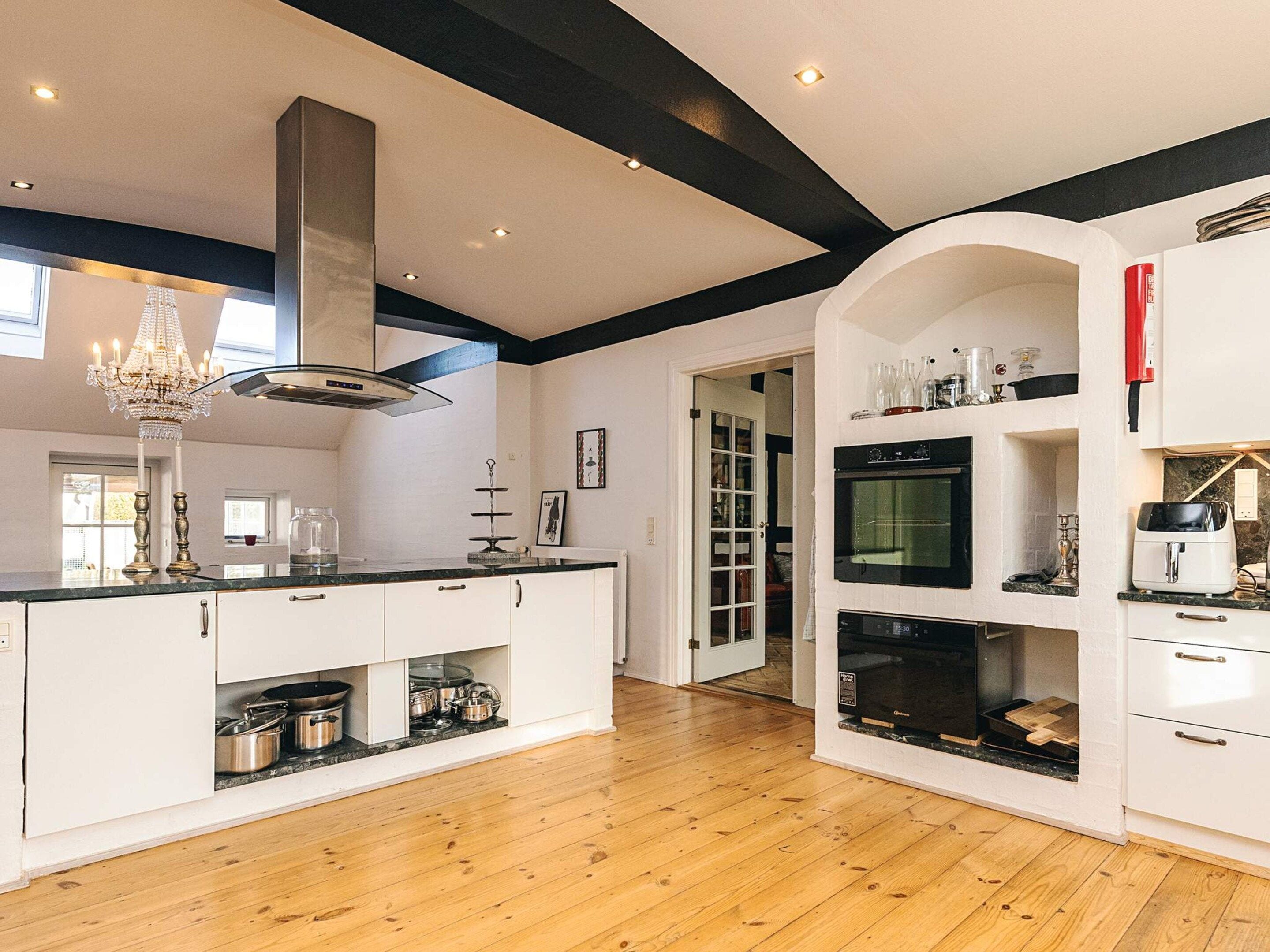 A modern kitchen with a central island, built-in oven, and a chandelier.