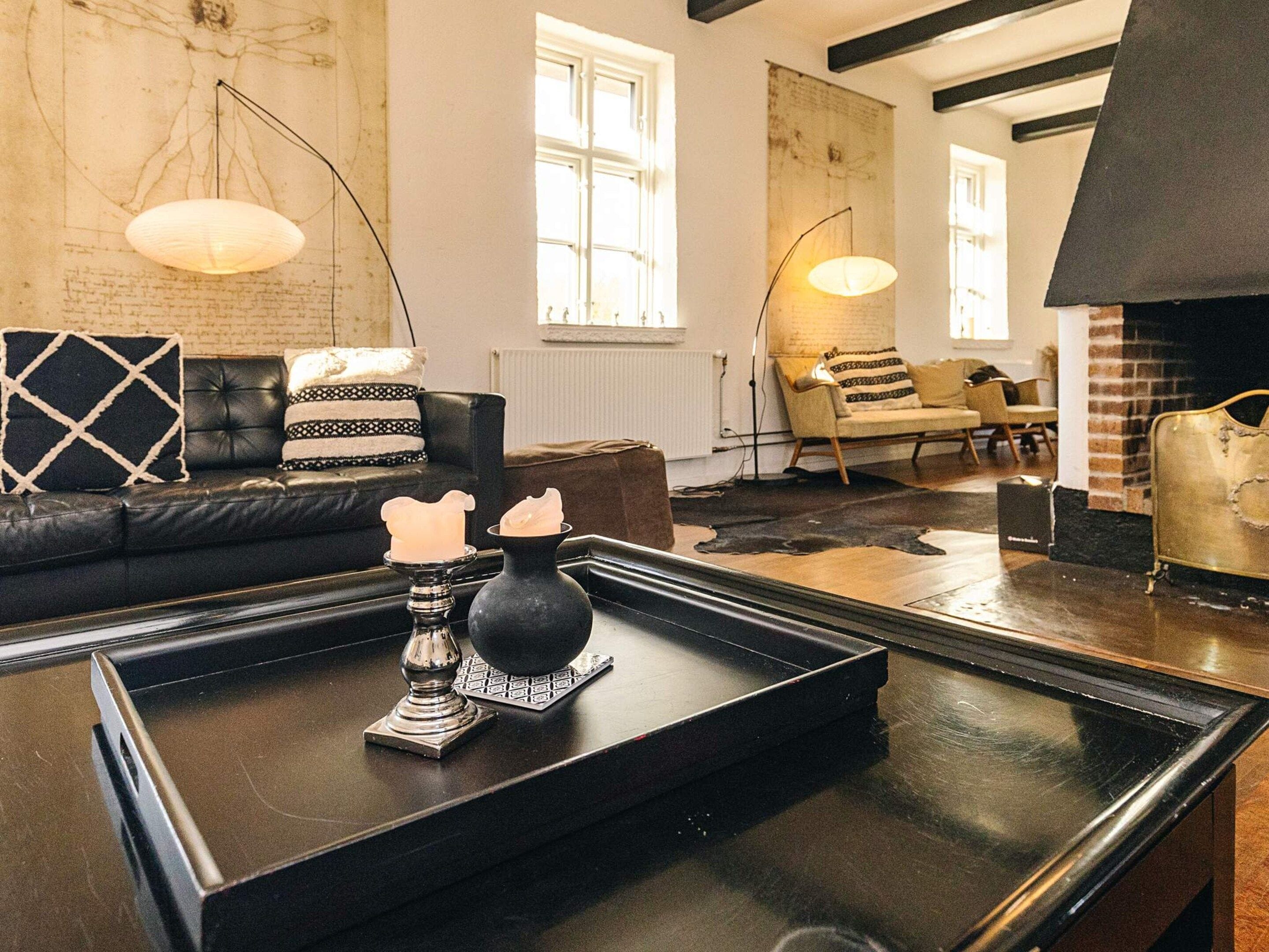 A modern living room with a black leather sofa, a coffee table with decorative items, and a fireplace.