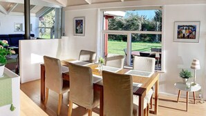 A modern dining area with a wooden table and chairs, large windows offering a view of the outdoors, and artwork on the walls.