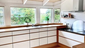 A modern kitchen with white cabinets, a wooden countertop, and a large window overlooking greenery.