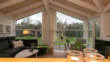 A modern living room with a wooden ceiling, a sofa, a coffee table, and a fireplace. There are three candles on a table.