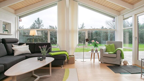 A spacious living room with a high ceiling, large windows, a sofa, a coffee table, and a chair.