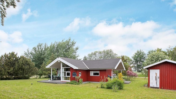 Une maison rouge à un étage, dotée d’un porche abrité, d’une petite remise attenante et d’une cour gazonnée.
