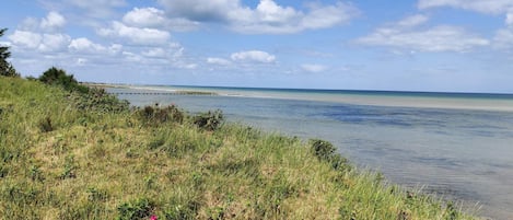 A coastal landscape with a grassy foreground, a calm sea, and a clear sky.