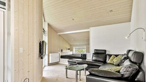 Een moderne woonkamer met een leren bank, een glazen salontafel en een aan de muur bevestigde televisie.