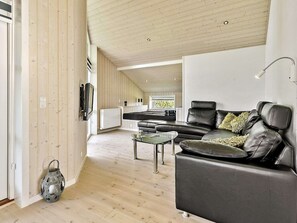 A modern living room with a leather sofa, a glass coffee table, and a TV mounted on the wall.