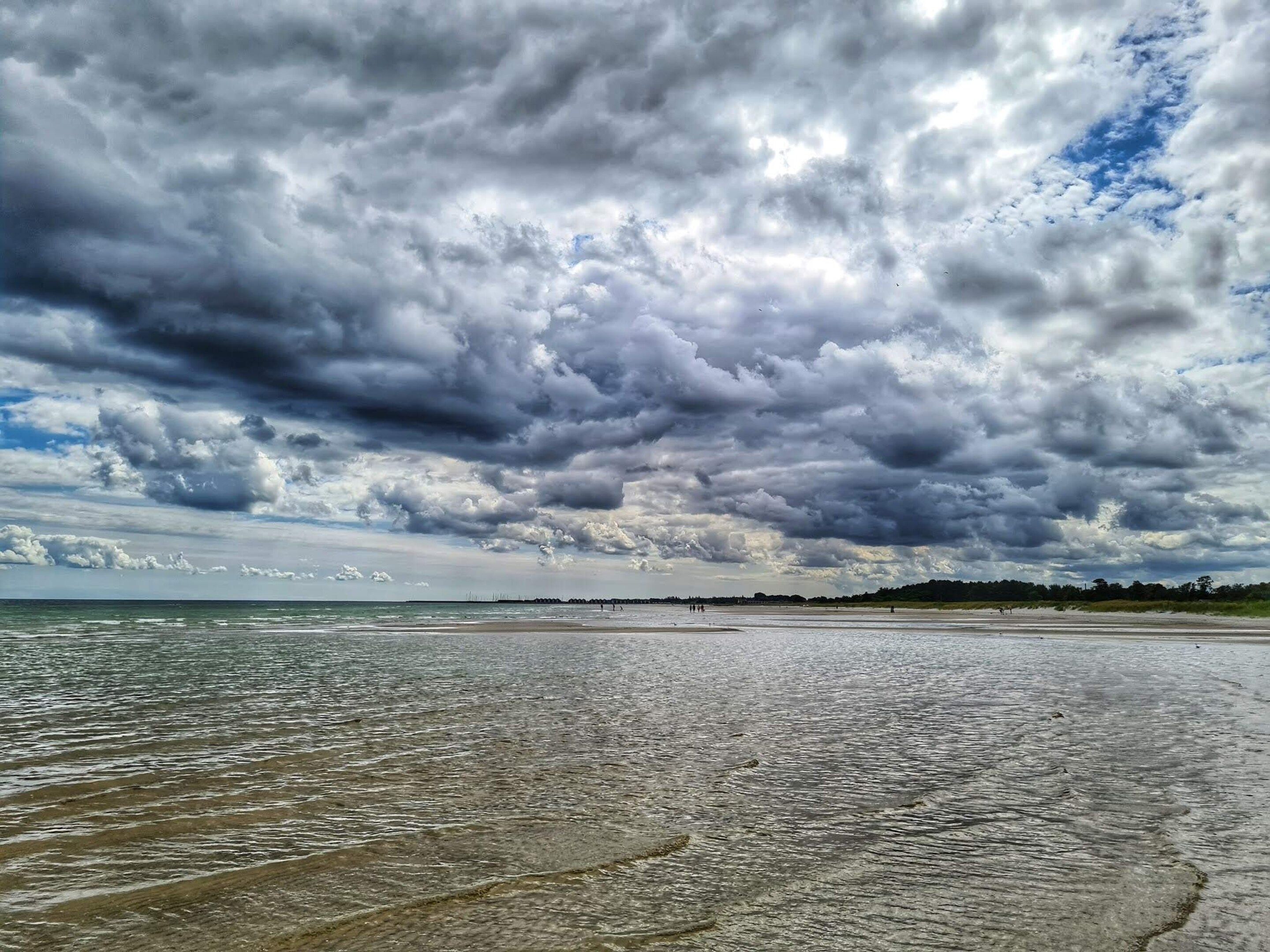 Uma praia com uma extensa faixa de areia e água, sob um céu nublado.