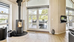 Een modern interieur met een houtkachel, grote ramen en een aan de muur bevestigde televisie.