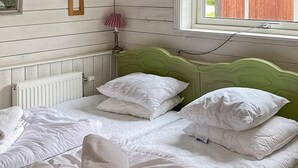 Una cama doble con ropa de cama y almohadas blancas, un cabecero verde, una lámpara de noche y una ventana con vistas a una valla de madera.