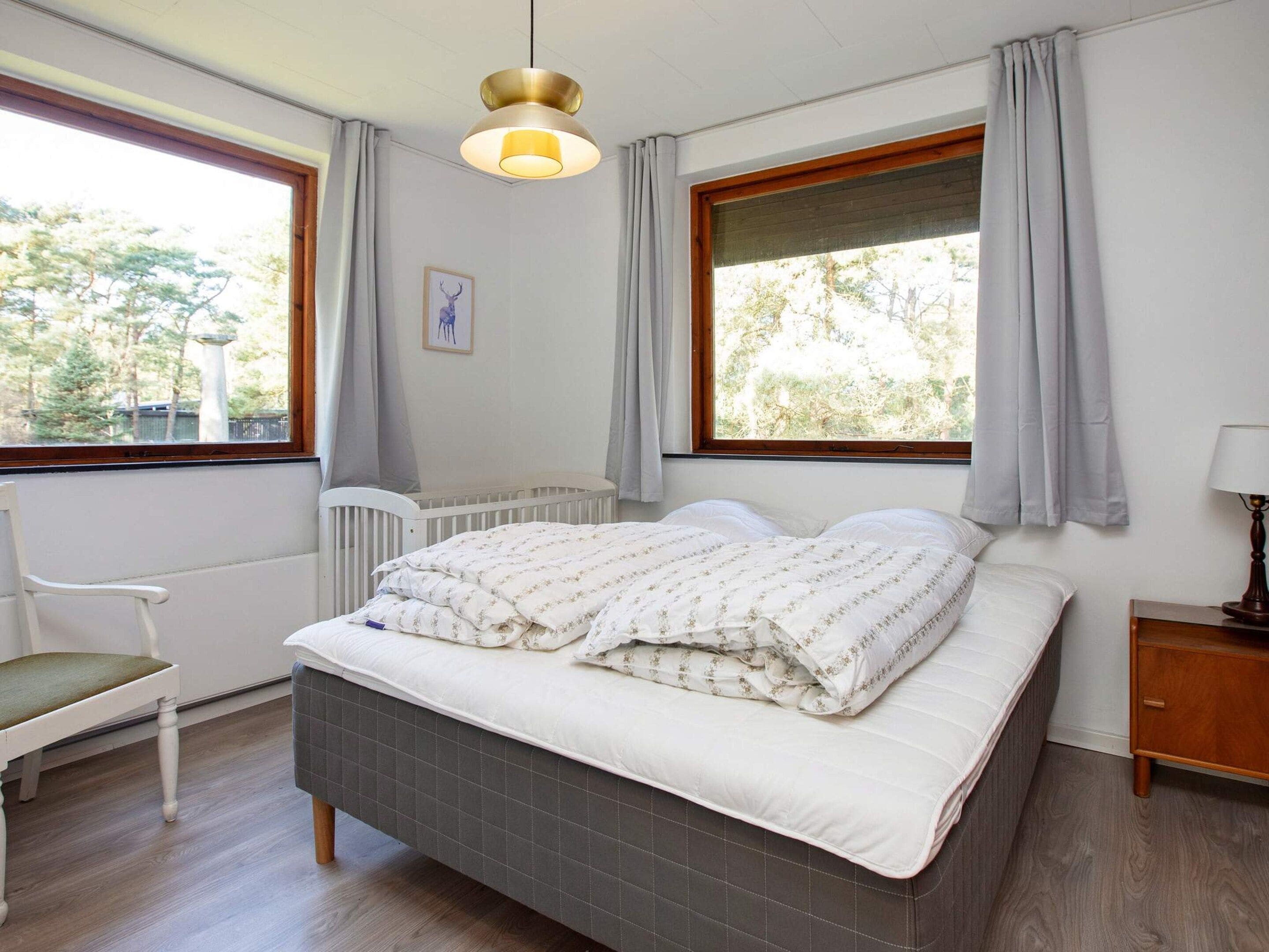 A bedroom with a bed, a chair, a bedside table, and a window with curtains.