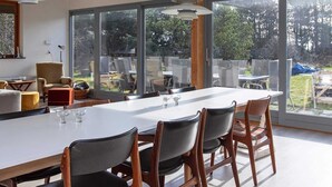 Uma área de jantar moderna com uma mesa grande, cadeiras e amplas janelas.