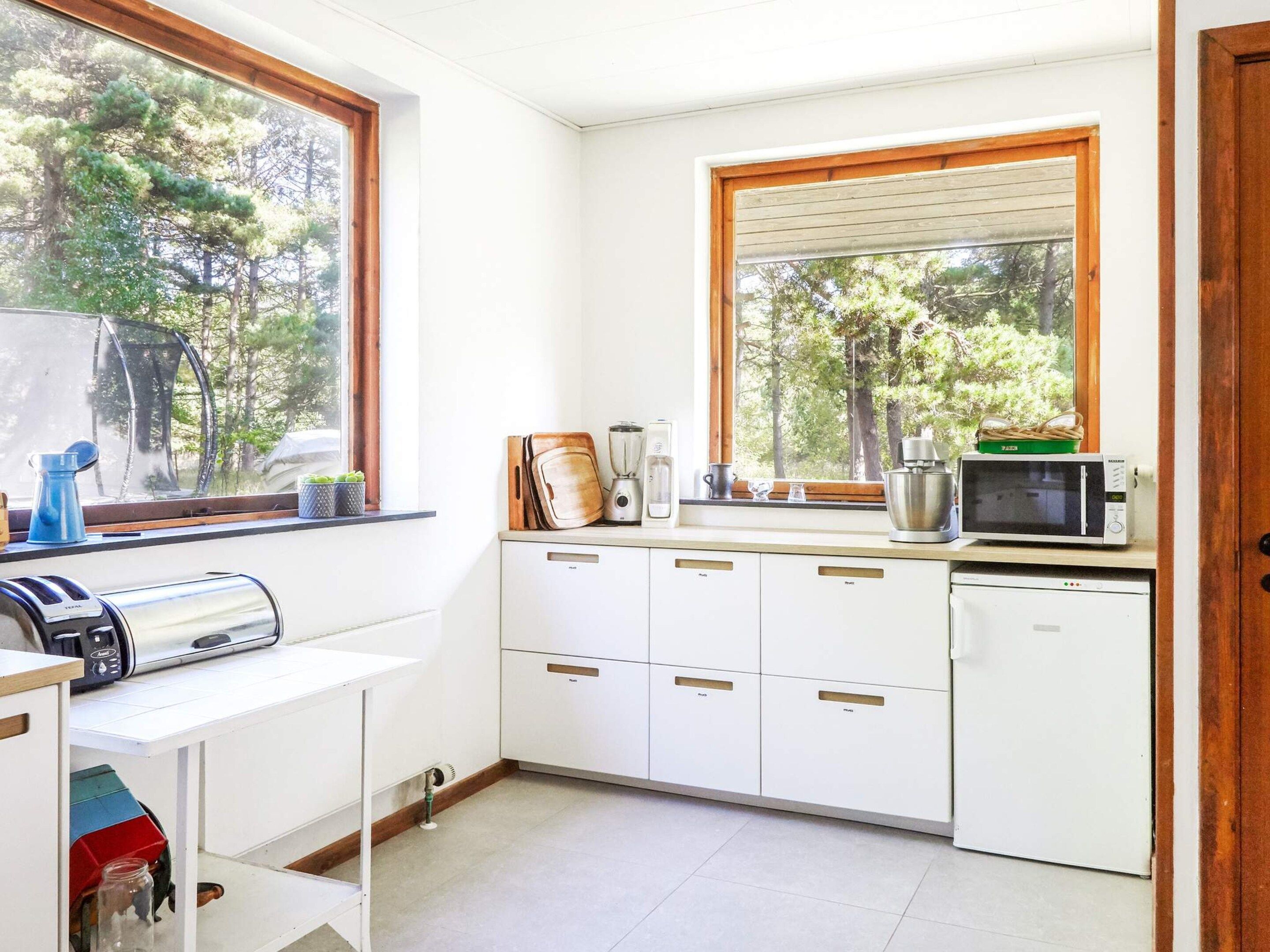 A compact kitchen with white cabinets, a built-in microwave, and a window with a view of trees.