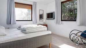 A bedroom with a bed, a TV, a window, and a chair.