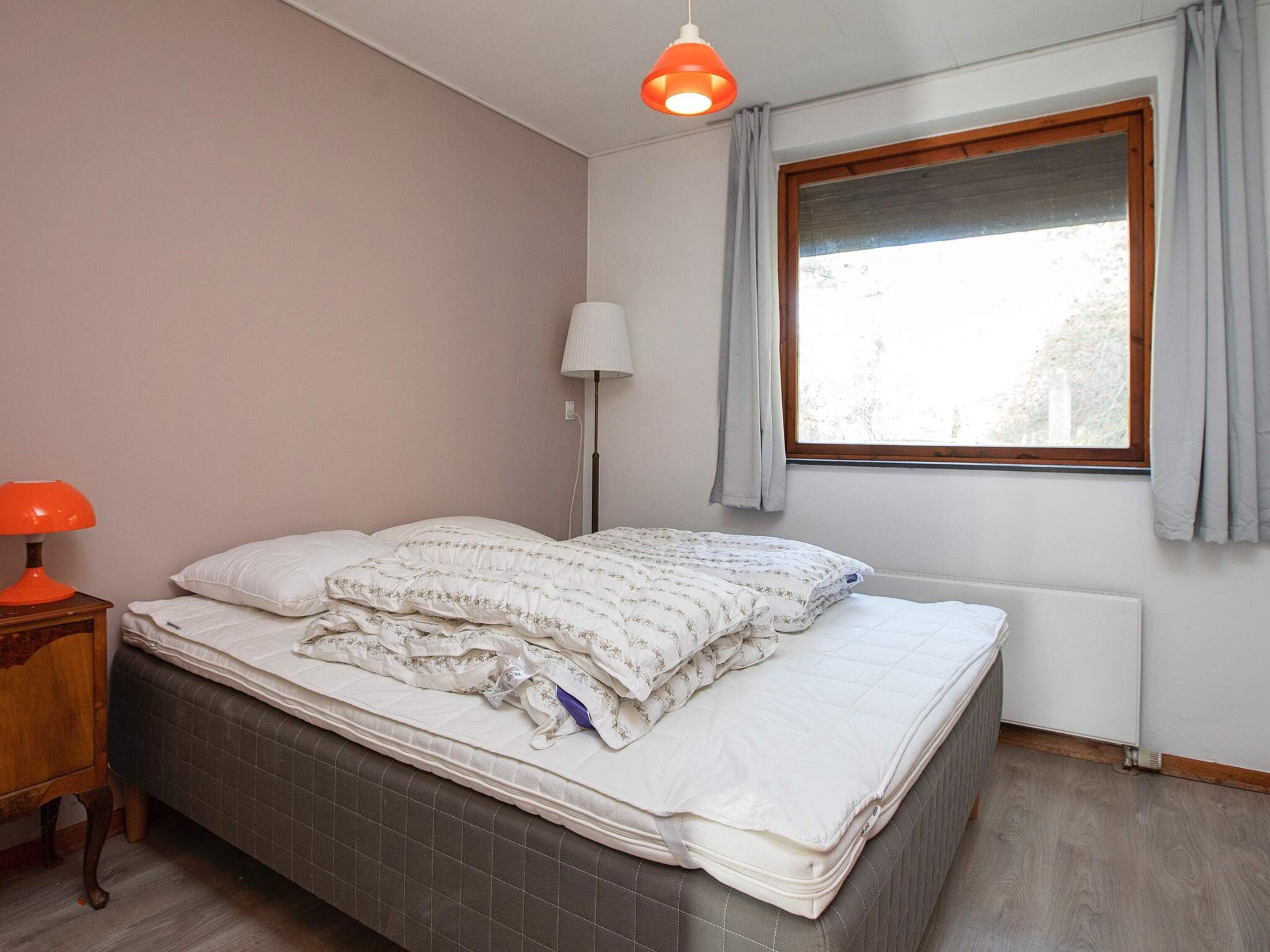 A bedroom with a bed, a nightstand, a lamp, a window with curtains, and a radiator.