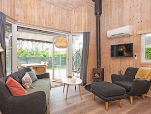 Una habitación acogedora con un sofá, un sillón y una pequeña mesa con una vela. Hay un ventanal y una puerta que da al exterior.
