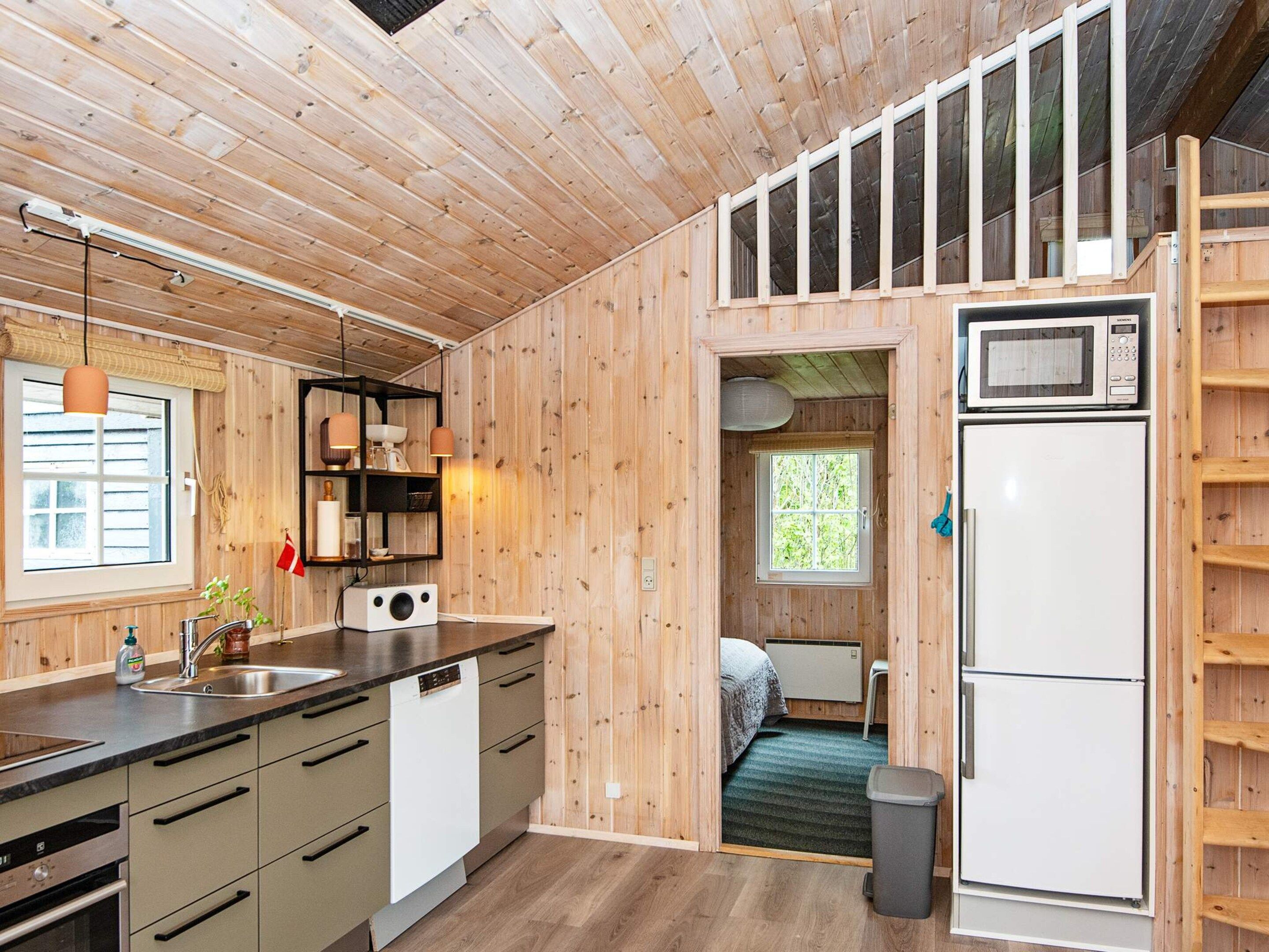 A compact kitchen with wooden walls, a built-in microwave, and a refrigerator.