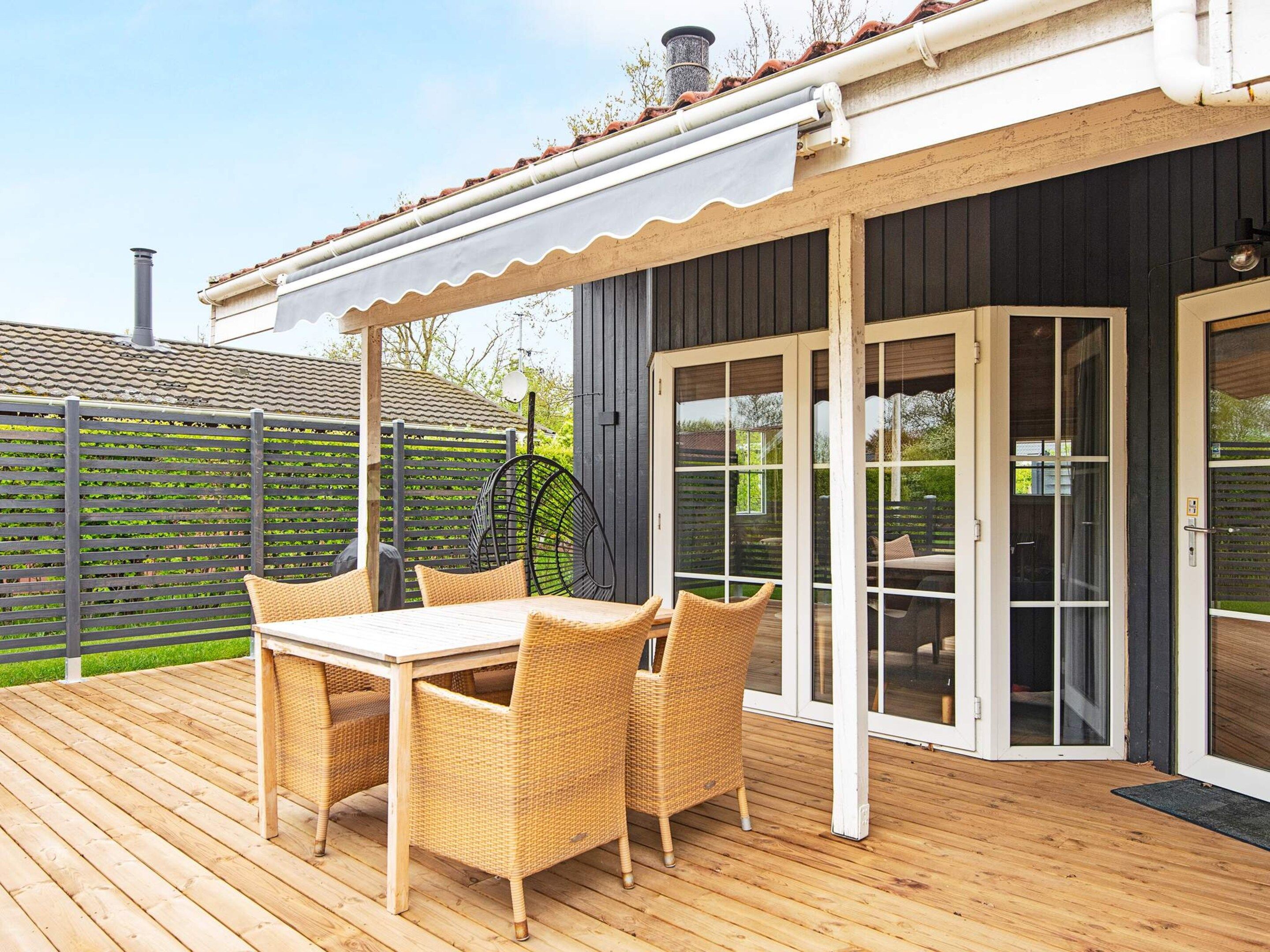 An outdoor patio with a wooden table and wicker chairs, a covered seating area, and a sliding glass door leading to an interior space.