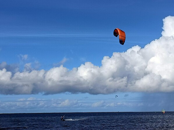 Vista del océano con una persona practicando windsurf y un kiteboarder a lo lejos.