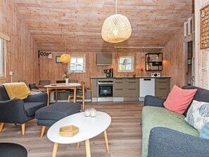 Hyggelig indretning med spiseområde, køkken og siddepladser, samt træloft og -vægge.