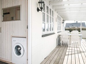 Fachada blanca e impecable de un edificio con terraza de madera, lavadora y una mesa con sillas.
