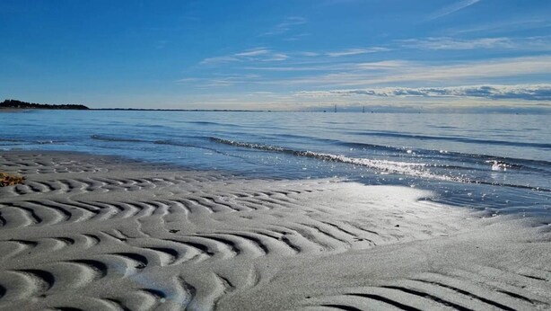 A beach with sand patterns and a calm sea under a clear sky.