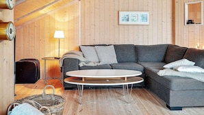 A cozy living room with a wooden ceiling, a grey sofa, a round coffee table, a lamp, and a framed picture on the wall.