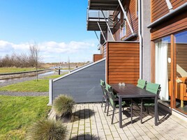 A modern outdoor patio with a table and chairs, a small garden area, and a view of a water body.