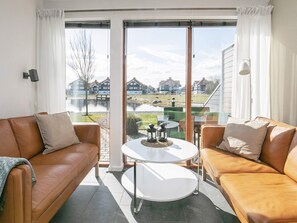 A modern living room with a glass door leading to a balcony, a white round table, and two brown leather sofas. - Holiday Home in Bogense (Bogense)