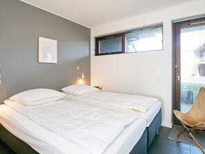 A bedroom with two beds, a bedside lamp, a framed picture on the wall, and a window with blinds. - Holiday Home in Bogense (Bogense)