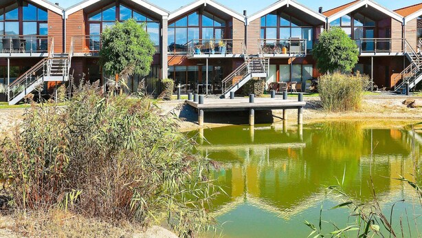 A row of modern, multi-story buildings with balconies, a dock, and a pond. - Holiday Home in Bogense (Bogense)