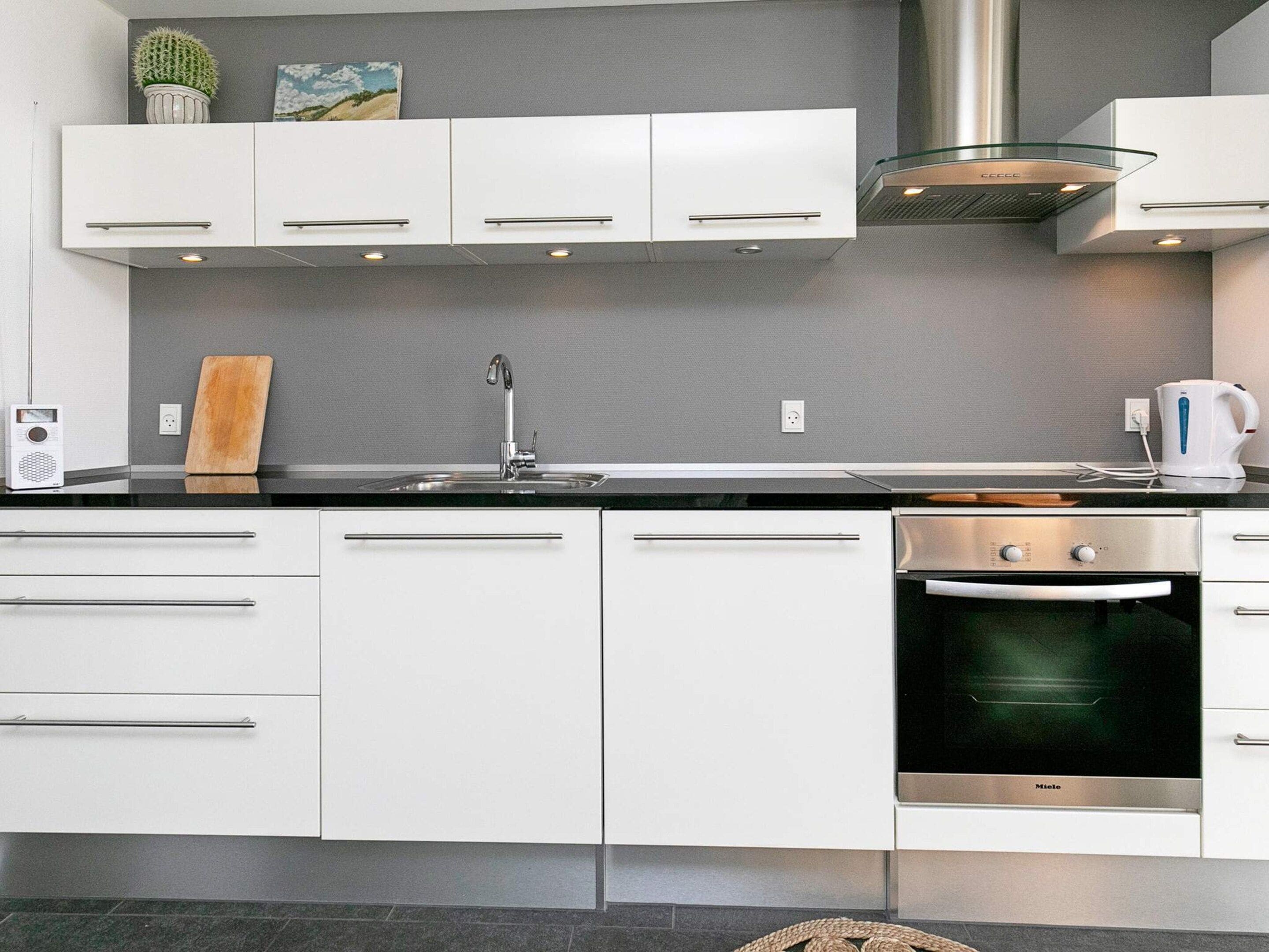 A modern kitchen with white cabinetry, a stainless steel range hood, a built-in oven, and a black countertop.