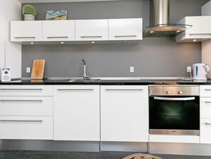 A modern kitchen with white cabinetry, a stainless steel range hood, a built-in oven, and a black countertop. - Holiday Home in Bogense (Bogense)
