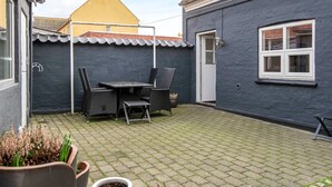 Une cour avec une table et des chaises, des plantes en pot et une porte.